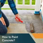 Painter applying durable concrete paint to a garage floor with a roller.